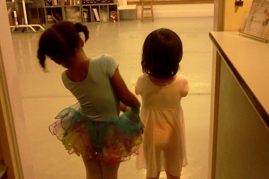 Two young dancers stand in the doorway of the studio watching older students in class
