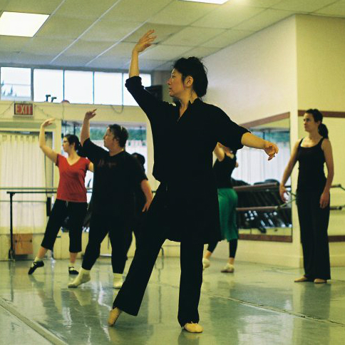 Adult dancers in class stand in ecarte
