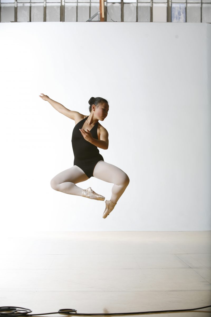One dancer in a black leotard mid jump