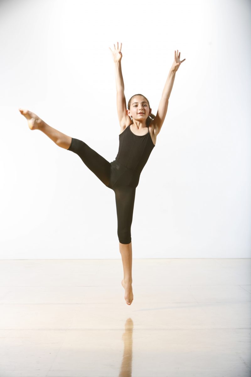 A young dancer in black mid jump
