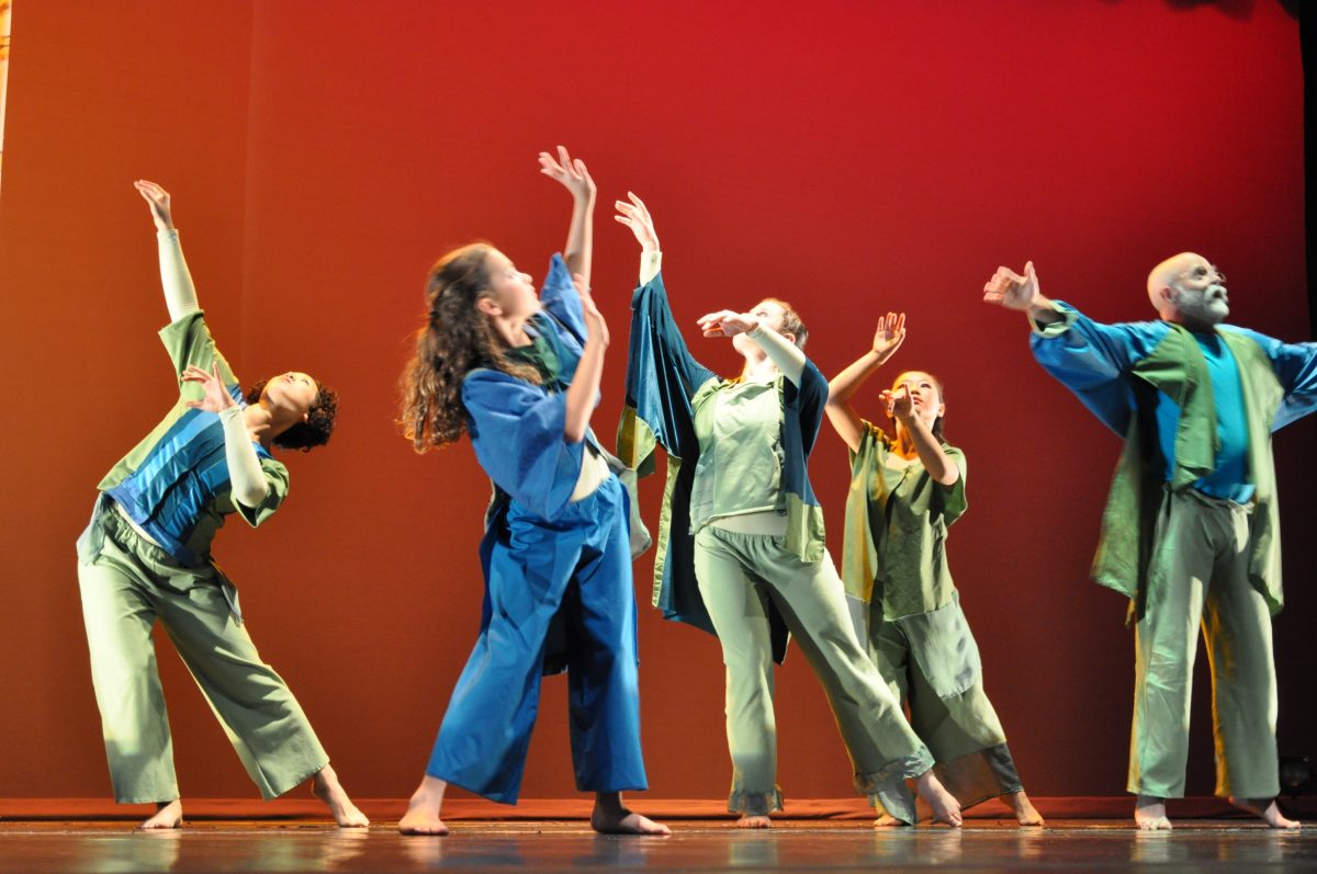 Dancers in green and blue costumes on stage in front of a red backdrop