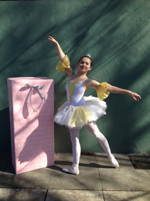 A teen dancer in costume poses next to a large, gift wrapped box before a Ballerina Birthday Party performance