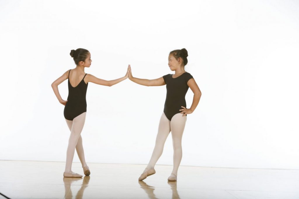 Two young dancers in tendu touching the palms of one hand together