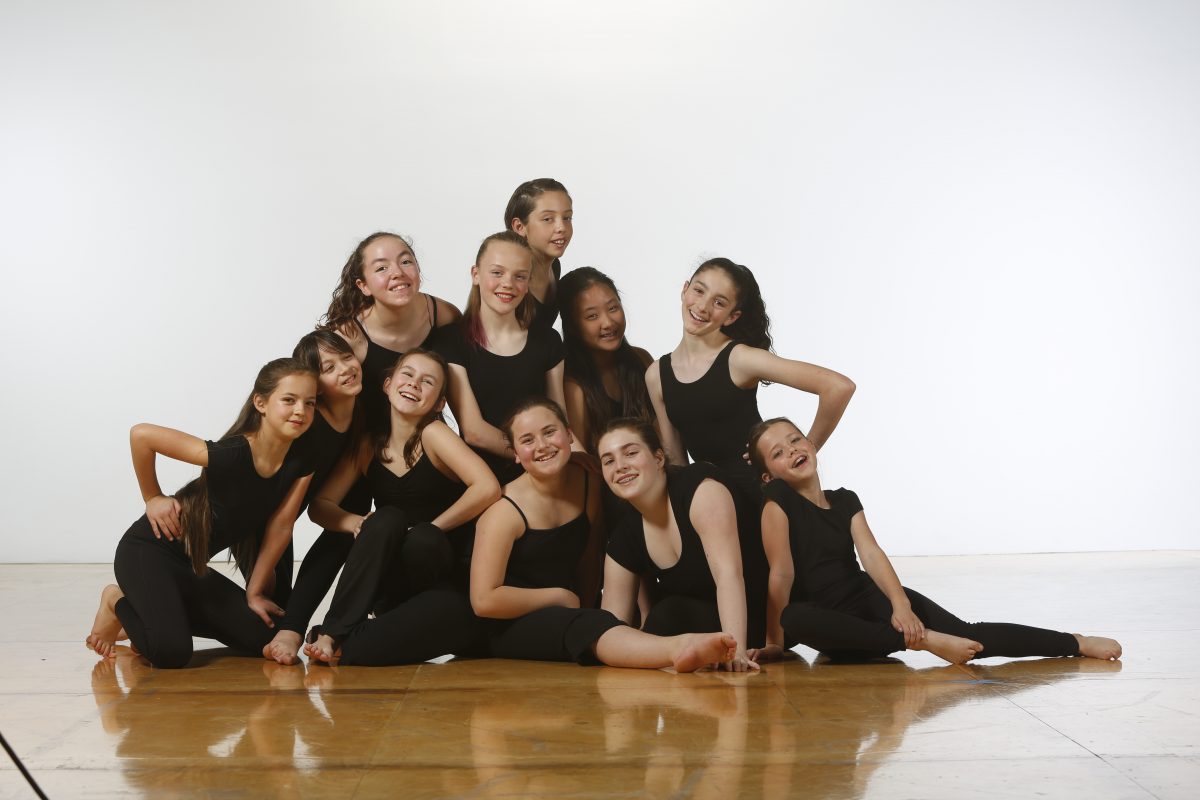 11 young dancers in all black pose casually