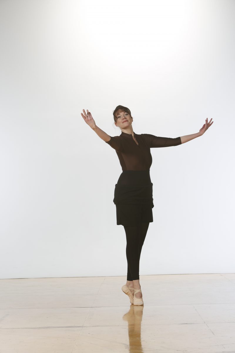 Adult dancer poses in sous-sous with arms stretched.