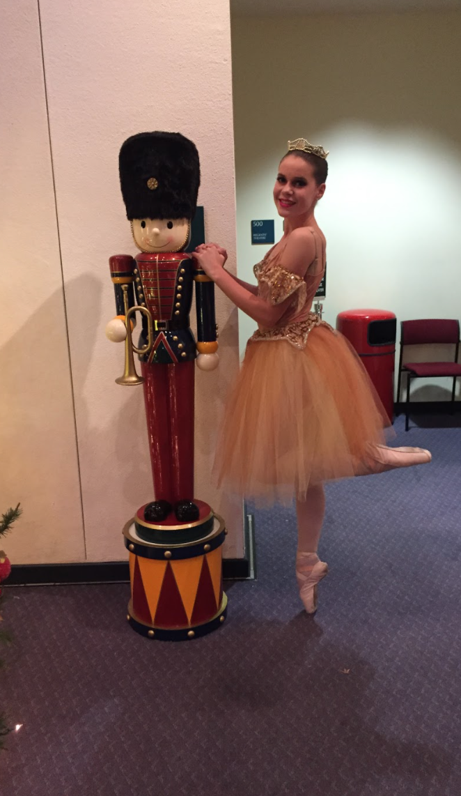 A dancer en pointe posing with a Nutracker in the lobby of a performance of the Nutcracker.