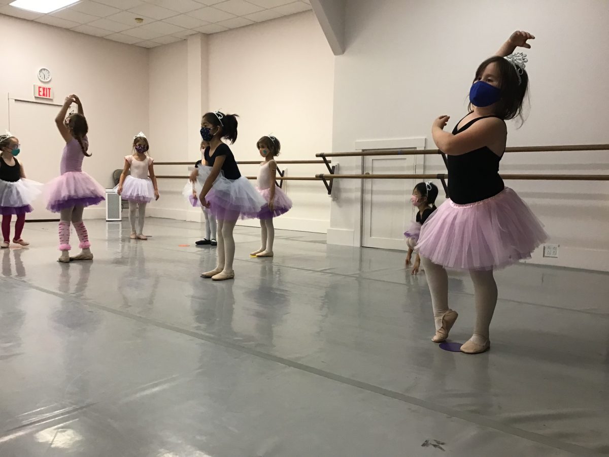 8 young dancers pictured in pink tutus, tiaras, and masks practicing a dance.