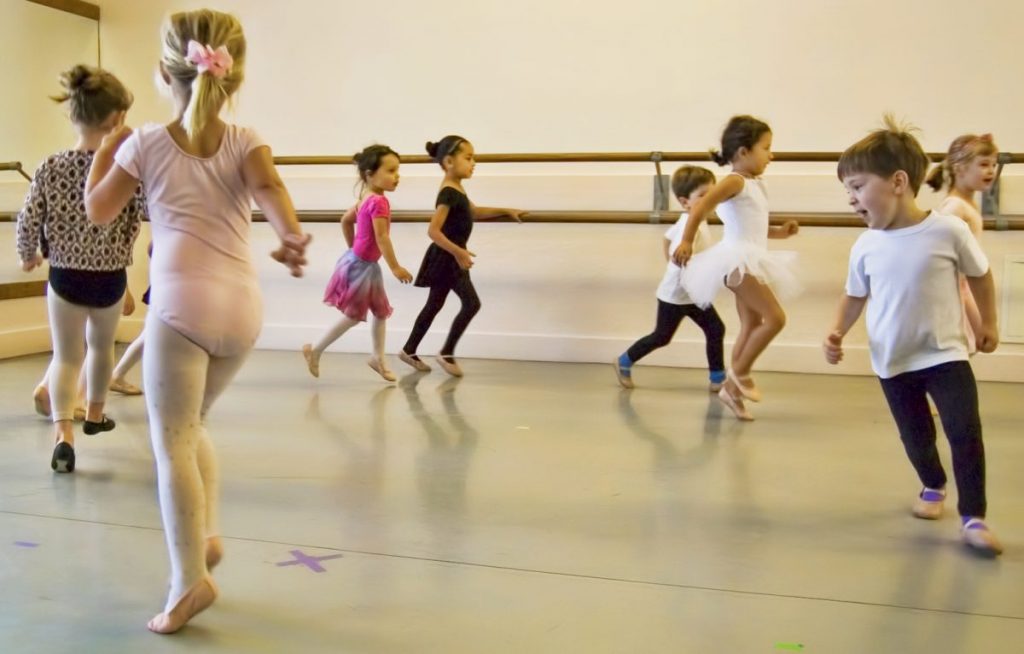 8 young dancers move in a large circle together in various outfit styles and colors.