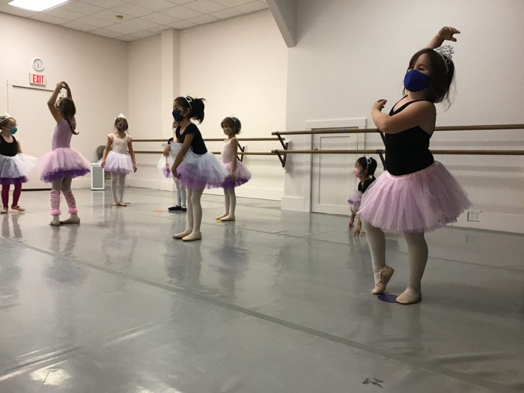 8 young dancers pictured in pink tutus, tiaras, and masks practicing a dance.