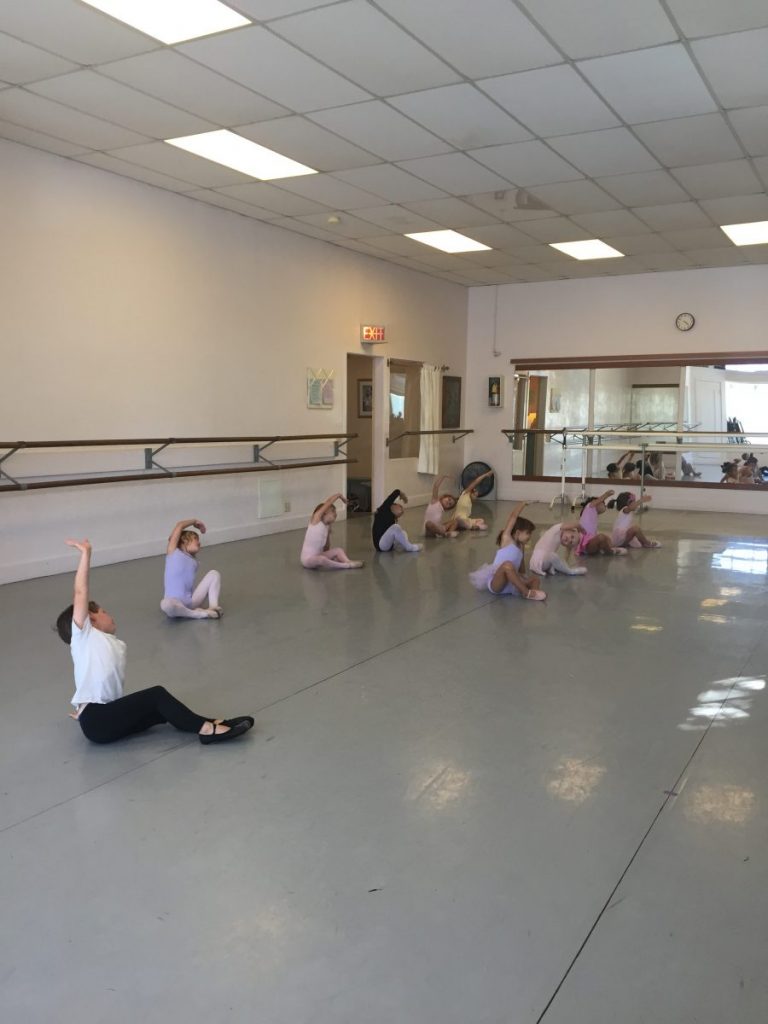 9 young dancers seated in the studio stretching to the side in Danspace's Studio 1